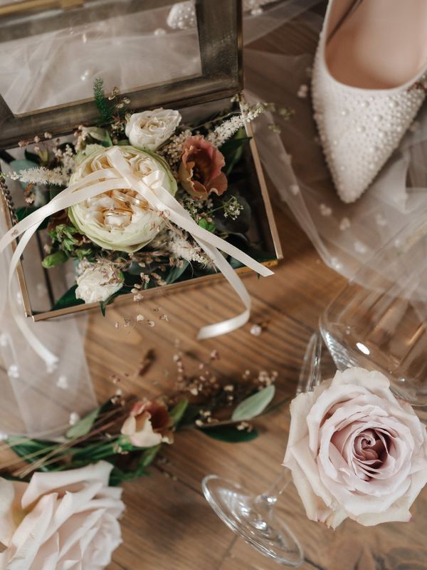 Eheringe in einer Glasbox mit Rosen und Brautschuhen